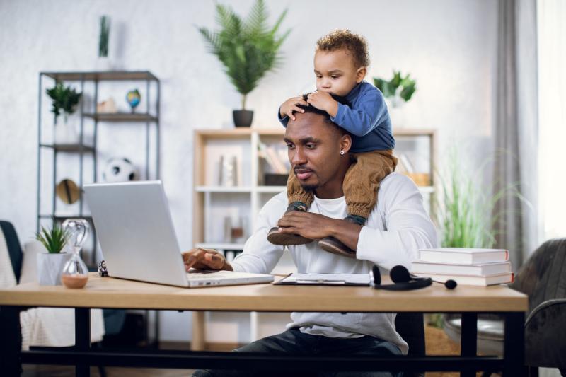a young boy sitting on his fathers shoulders while he looks at a laptop
