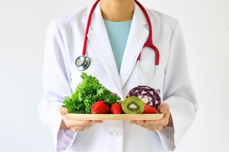 a person in a doctor coat holding a plate of vegetables and fruit